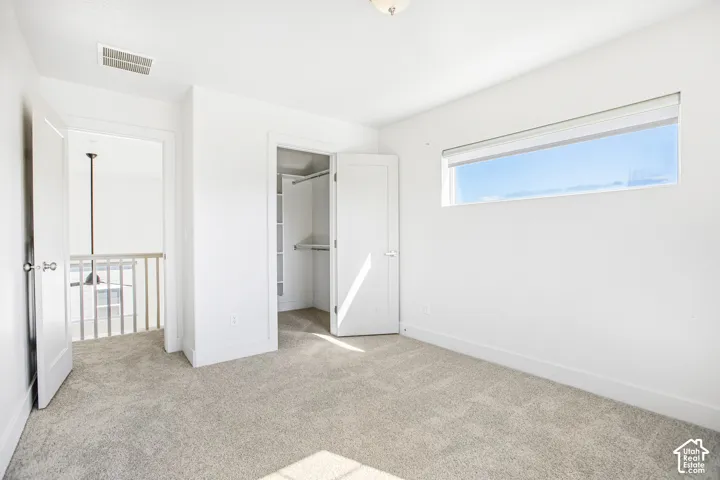 Room featuring neutral carpeting, a horizontal clerestory window, and a walk-in closet with built-in shelving