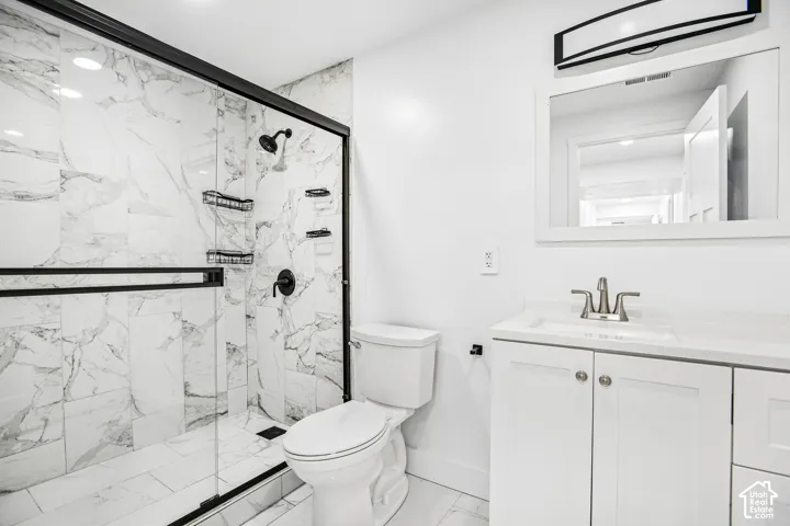 Bathroom featuring a walk-in shower with matte black hardware, stone-pattern tile surrounds, a white vanity with a composite countertop, and an integrated vanity mirror with task lighting