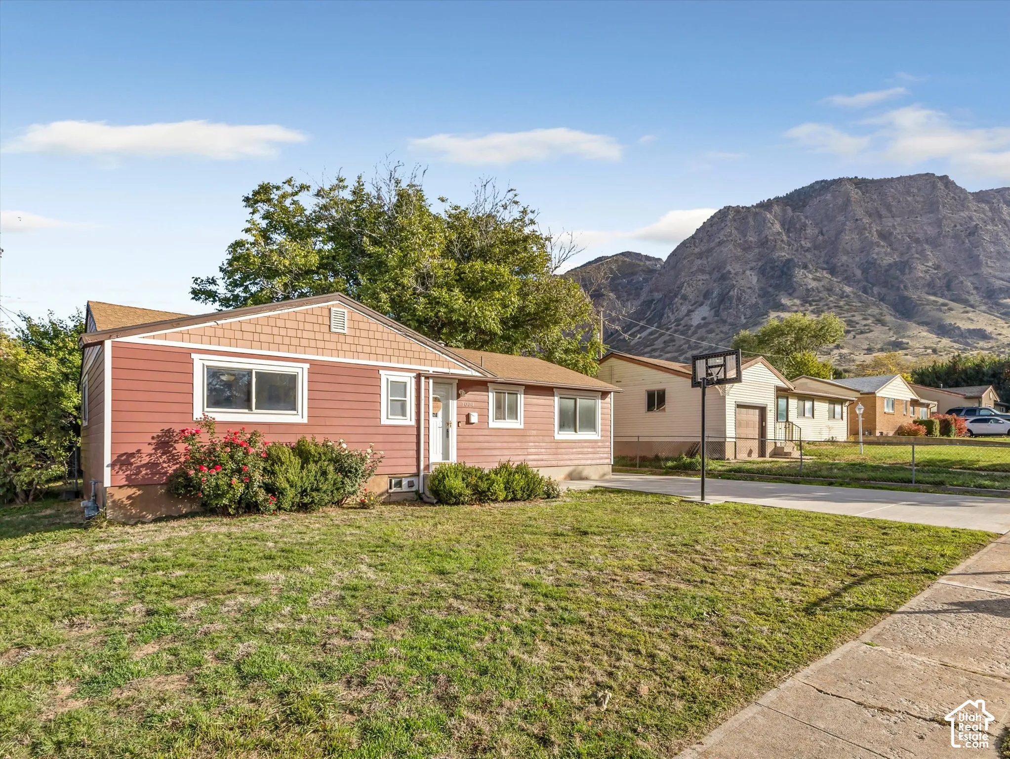 Single-story residence featuring horizontal lap siding, a shingled gable roof, and a concrete driveway, set against a prominent mountain backdrop
