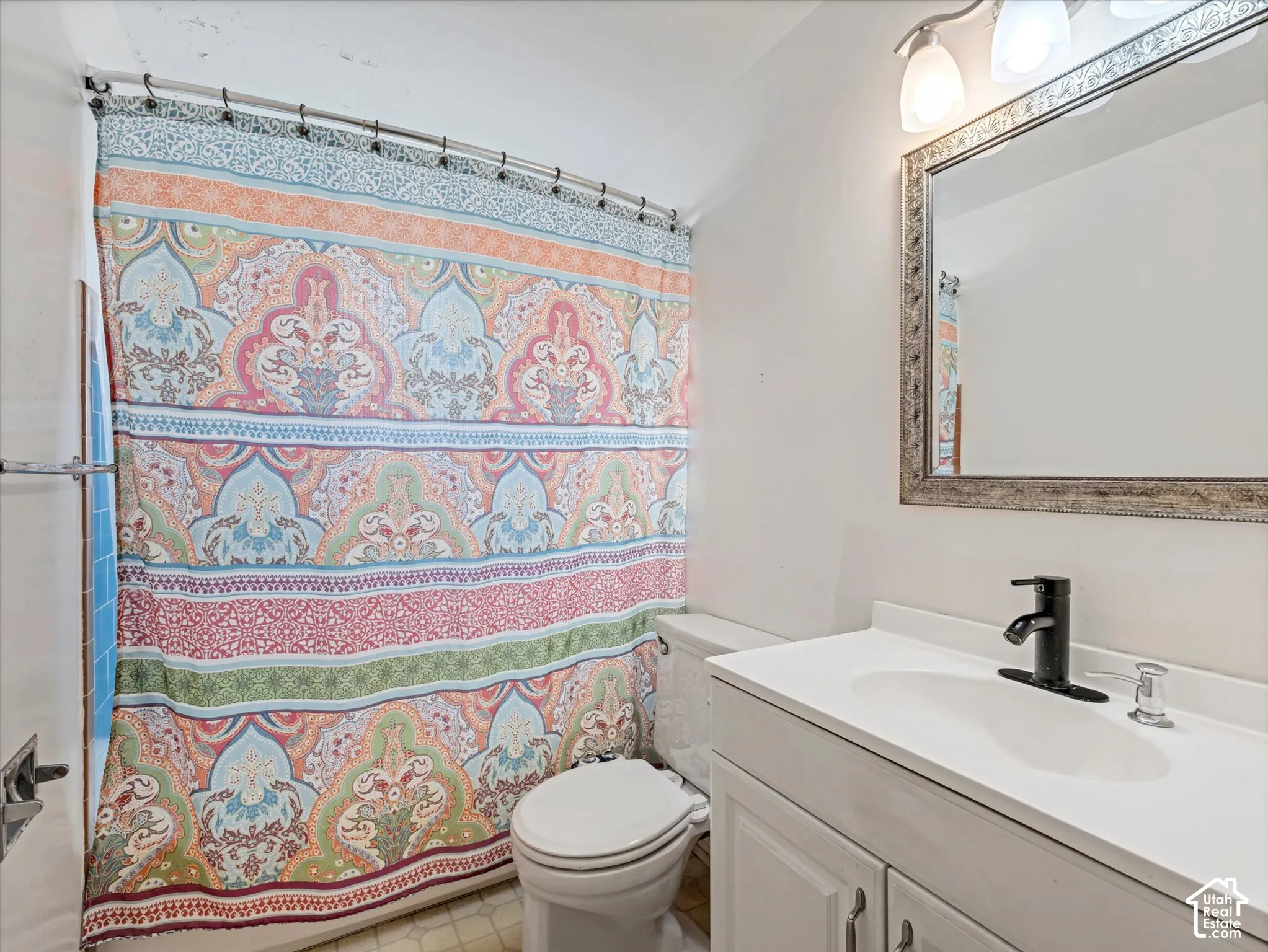 Bathroom featuring a white vanity cabinet with an integrated white sink, matte black faucet, wall-mounted light fixture, and framed mirror