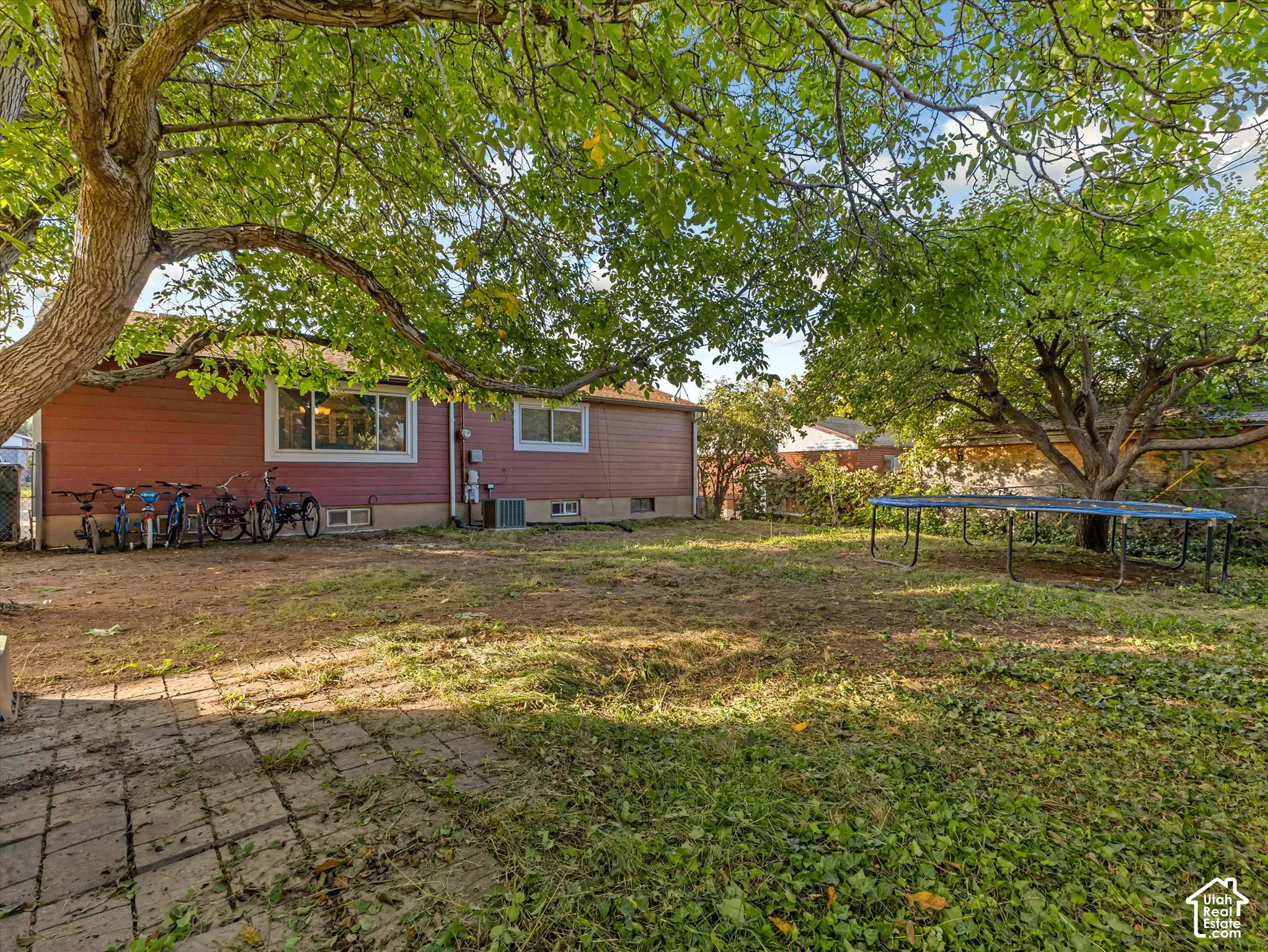 Exterior features include red horizontal siding, a stone paver patio, and mature trees providing shade across the grounds
