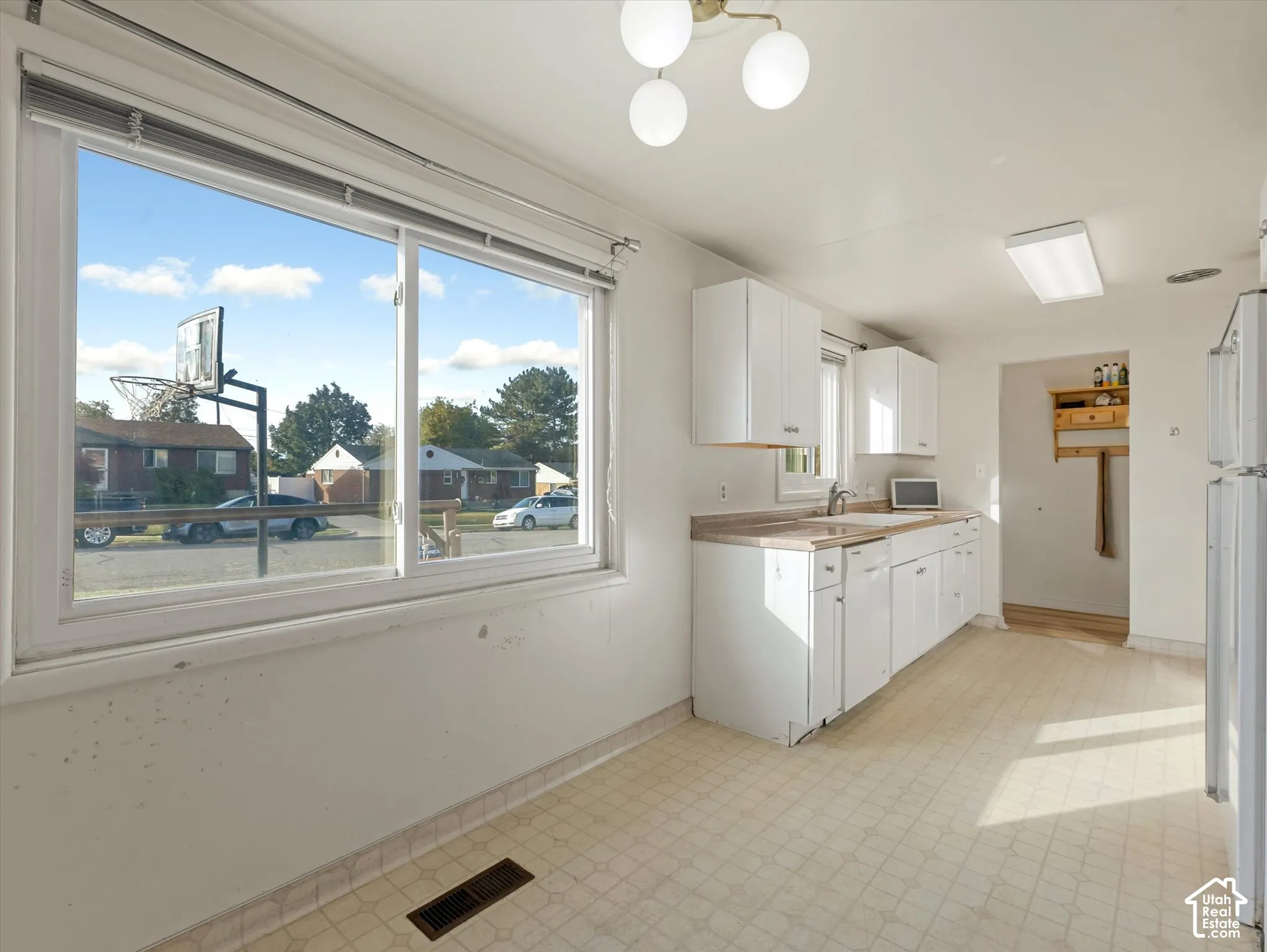 Kitchen featuring white cabinetry, light-toned laminate countertops, a dual-basin sink, resilient vinyl flooring, and a large horizontal window providing natural light