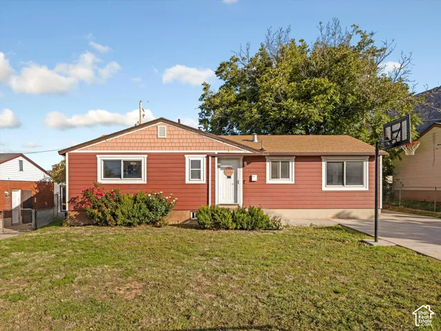 Single-story exterior featuring red horizontal siding, shingle-style gable detailing, a concrete driveway, and established landscaping
