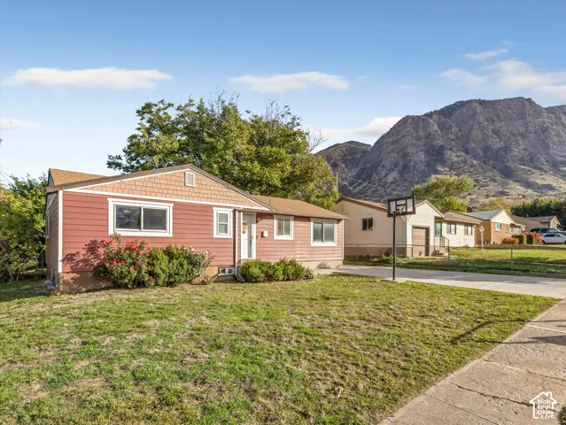 Single-story residence featuring horizontal lap siding, a shingled gable roof, and a concrete driveway, set against a prominent mountain backdrop