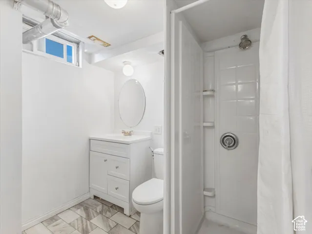 Bathroom featuring a vanity with integrated sink, oval wall-mounted mirror, white tile shower surround, and patterned tile flooring