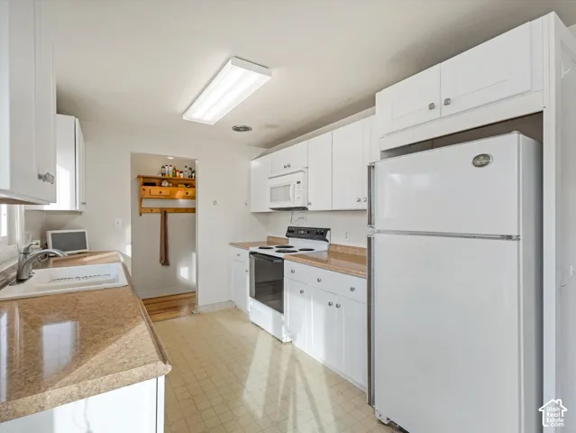 Kitchen featuring white cabinetry, stone-finish countertops, an integrated microwave, a top-mount sink, and a built-in wall shelf