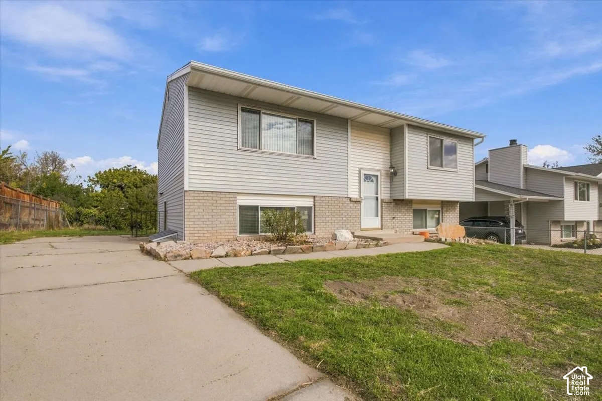Split-level exterior featuring light-gray horizontal siding, a masonry brick facade, an attached carport, and a concrete driveway