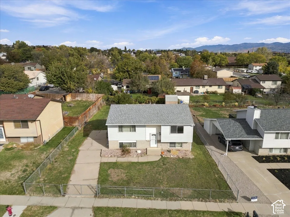 Split-level residence featuring a gray asphalt shingle roof, neutral siding, concrete driveway, and a chain-link fenced perimeter