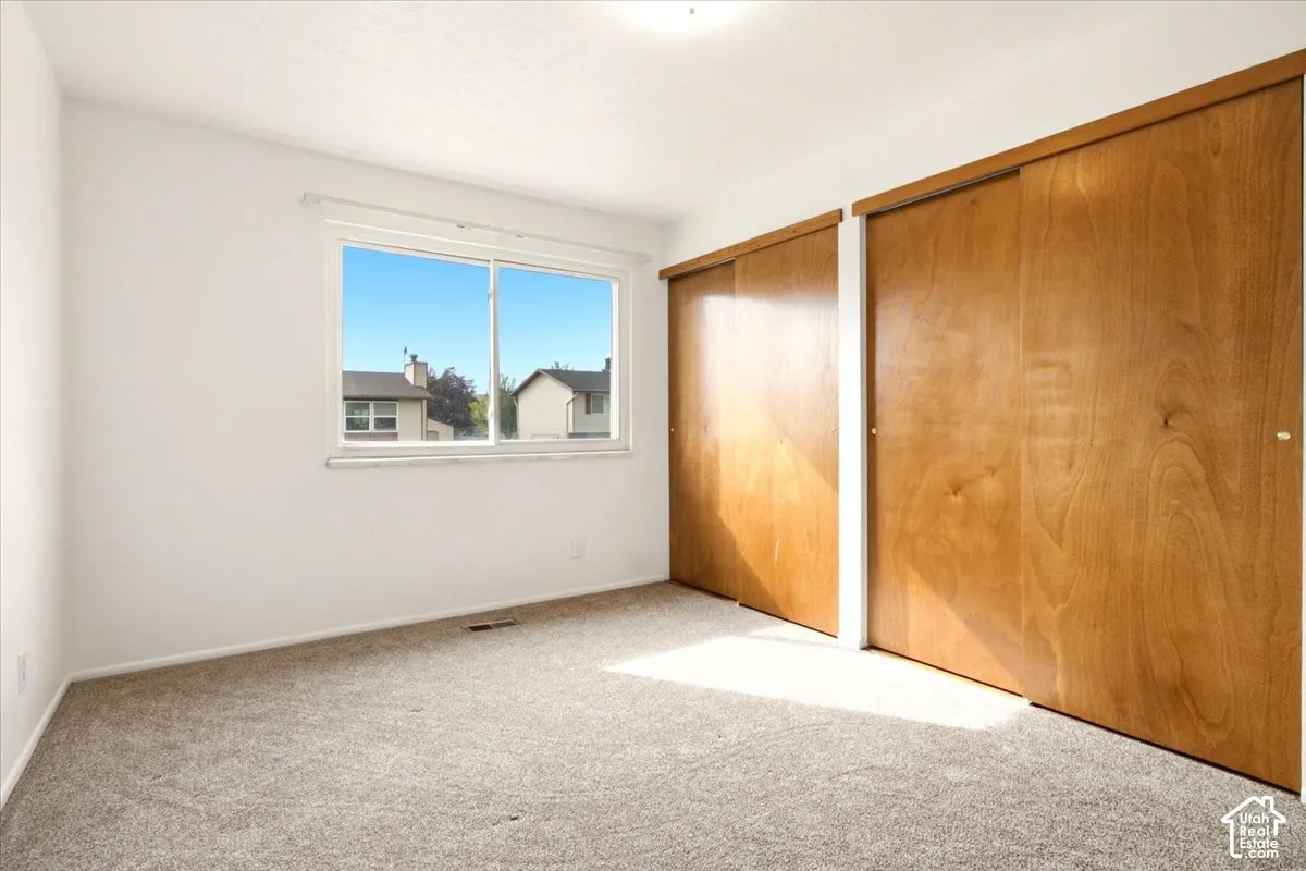 Room featuring neutral carpeting, a dual-pane sliding window, and dual sliding closets with wood-finish doors
