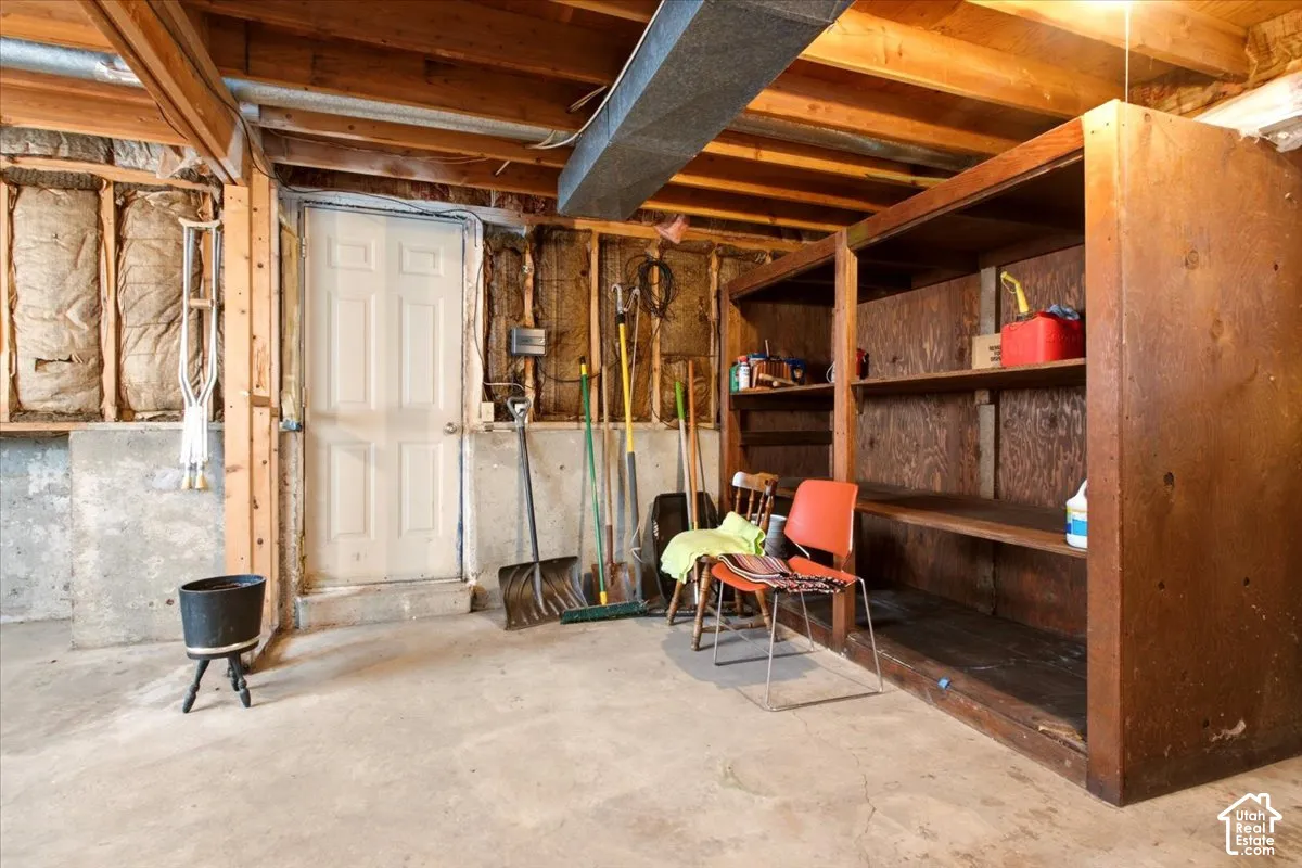 Unfinished storage area featuring exposed wood joists, concrete foundation walls, built-in plywood shelving, and a six-panel door