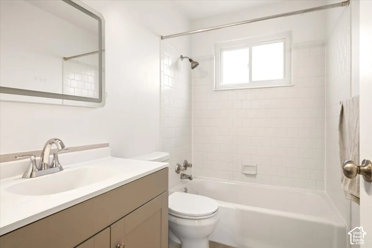 Bathroom featuring a vanity with an integrated sink, rectangular wall-mounted mirror, white subway tile shower surround, and a sliding window
