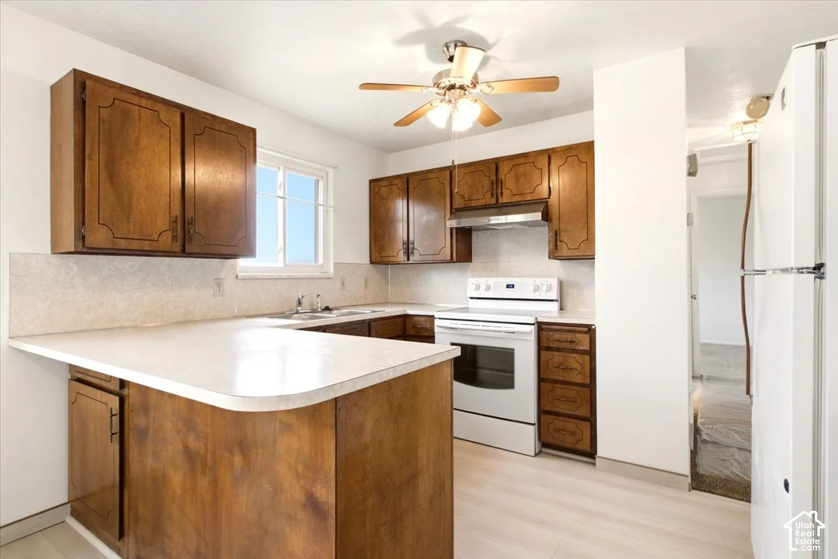 Kitchen featuring wood cabinetry, white laminate countertops, light-toned wood-finish flooring, a built-in exhaust hood, and a ceiling fan with integrated lighting