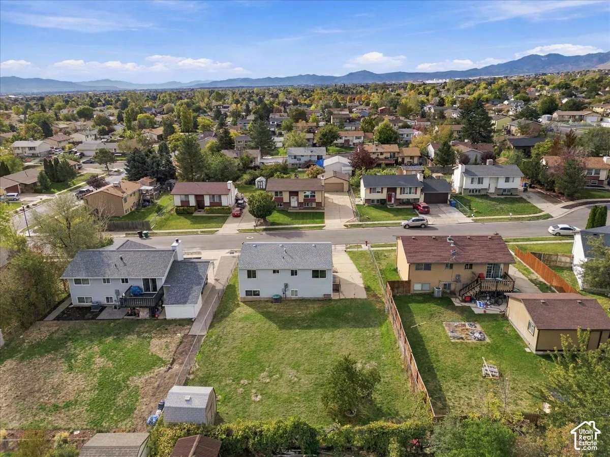 Aerial perspective of a residential property featuring a large backyard, lawn area, perimeter fencing, and a mountain range backdrop