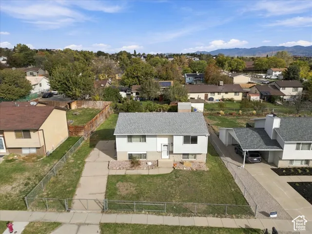 Split-level residence featuring a gray asphalt shingle roof, neutral siding, concrete driveway, and a chain-link fenced perimeter