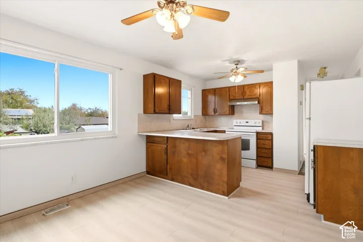 Kitchen featuring wood cabinetry, solid-surface countertops, light-toned wood-finish flooring, and dual ceiling fans