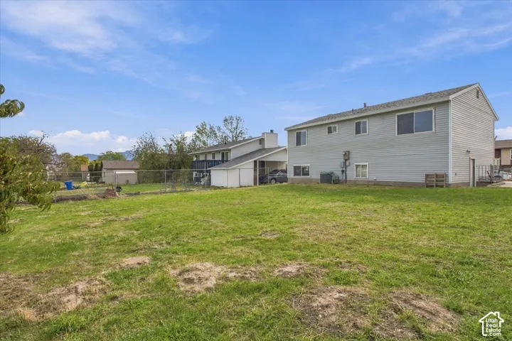 Expansive backyard featuring a large grass lawn, chain-link perimeter fencing, and multi-story residence with light-colored siding