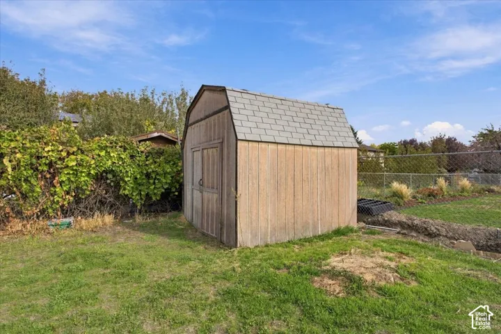 Storage shed featuring vertical wood-finish siding, a gambrel roof with asphalt shingles, and double-door entry