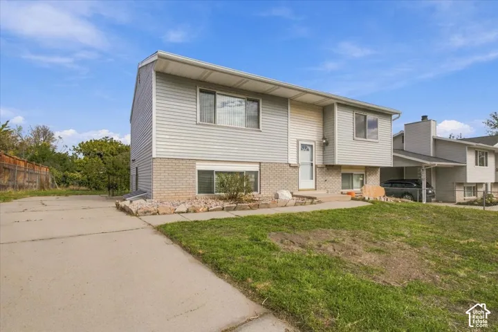Split-level exterior featuring light-gray horizontal siding, a masonry brick facade, an attached carport, and a concrete driveway