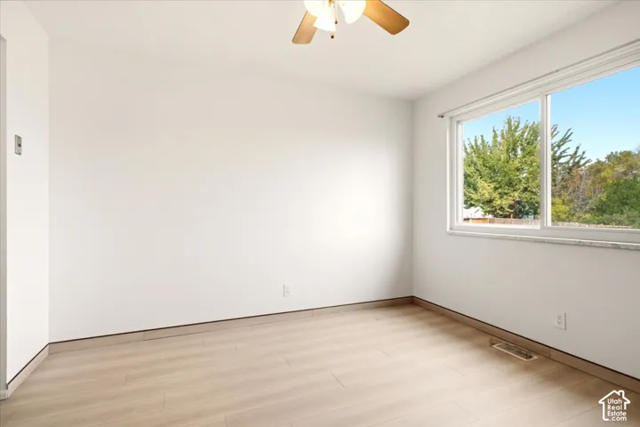 Room featuring wood-finish flooring, a large sliding window, a neutral wall finish, and a ceiling fan