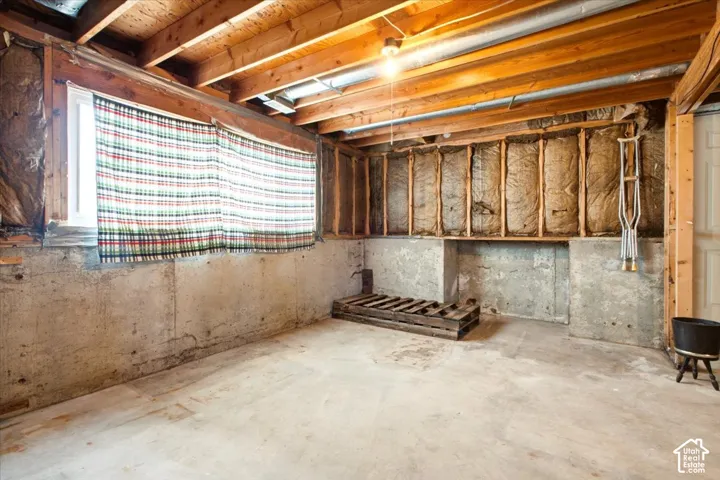 Unfinished lower-level space featuring concrete walls, exposed ceiling joists, insulation, and a window