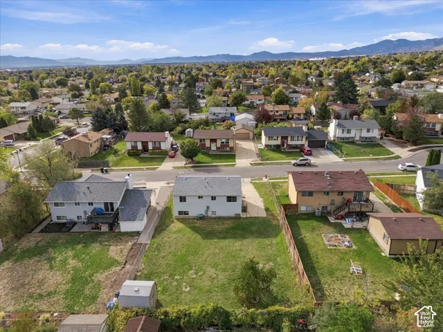 Aerial perspective of a residential property featuring a large backyard, lawn area, perimeter fencing, and a mountain range backdrop