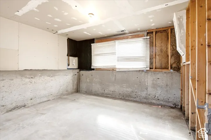 Unfinished room featuring exposed concrete foundation walls, stud framing, partial drywall installation, and a horizontal window