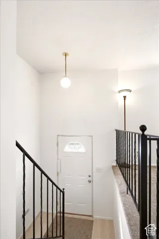 Entryway featuring a white exterior door with a semi-circular transom window, black iron railing, and a globe pendant light fixture