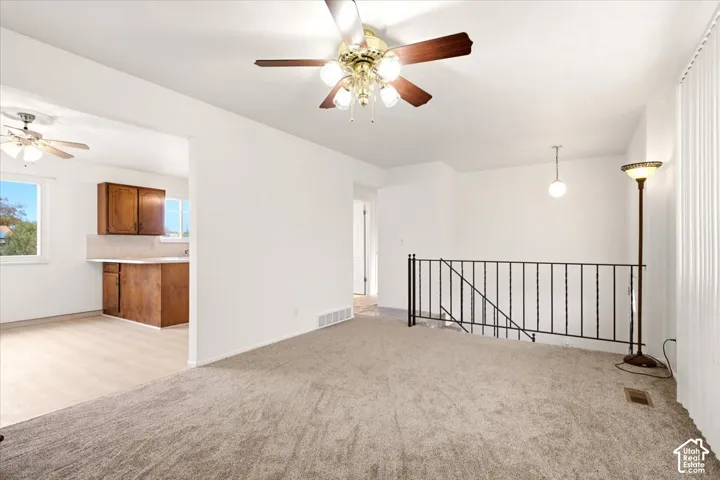 Interior space featuring neutral-toned carpeting, a ceiling fan with multi-light fixture, and black metal stair railing