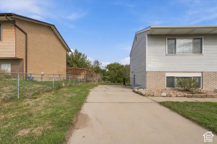 Concrete driveway flanked by grass, chain-link fencing, and horizontal siding exterior