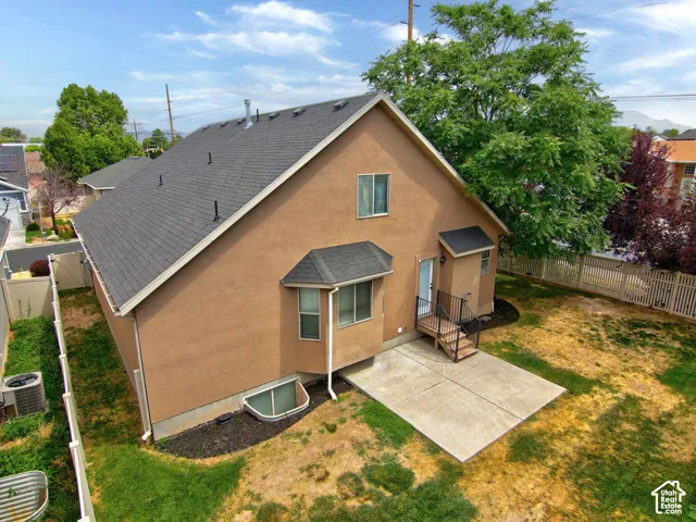 Stucco exterior featuring an asphalt shingle roof, concrete patio, metal staircase, and fenced perimeter