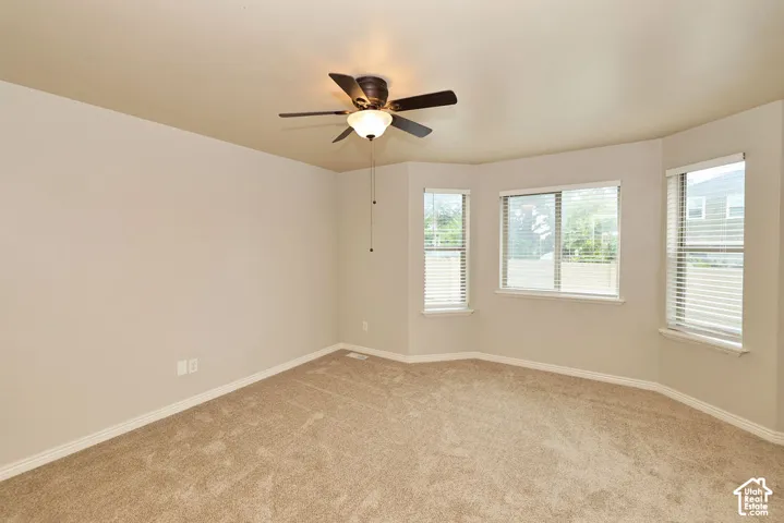 Neutral interior featuring plush wall-to-wall carpeting, three-panel bay windows, and a ceiling fan with integrated lighting