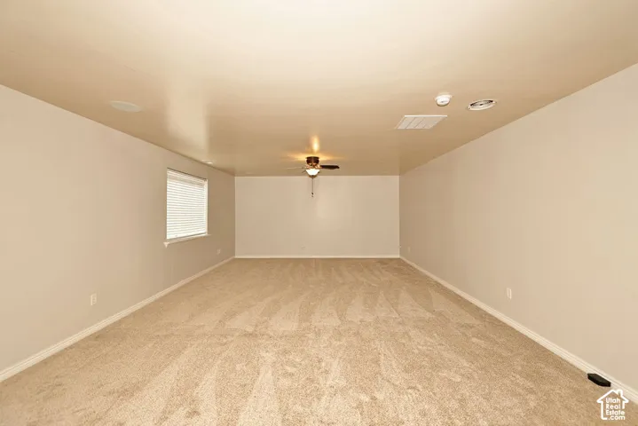 Spacious room featuring neutral carpeting, a ceiling fan with integrated lighting, and a single window with blinds
