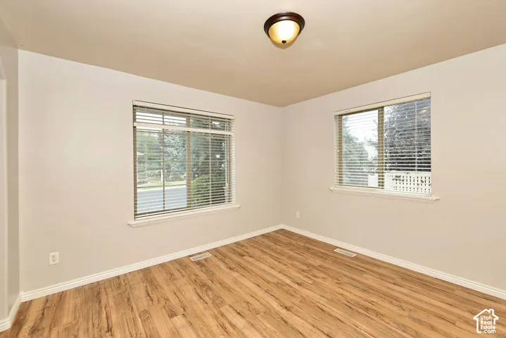 Neutral-toned interior space featuring wood-finish flooring, dual windows with horizontal blinds, and a circular flush-mount ceiling light fixture