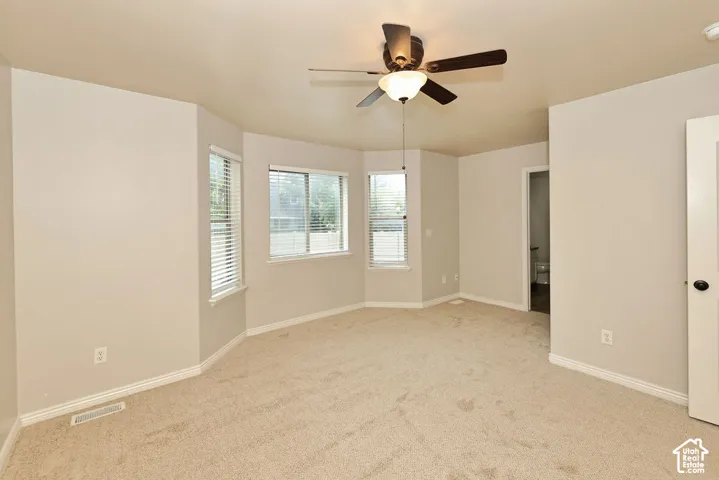 Interior room featuring neutral wall tones, wall-to-wall carpeting, three bay-style windows, and a ceiling-mounted light fixture with integrated fan