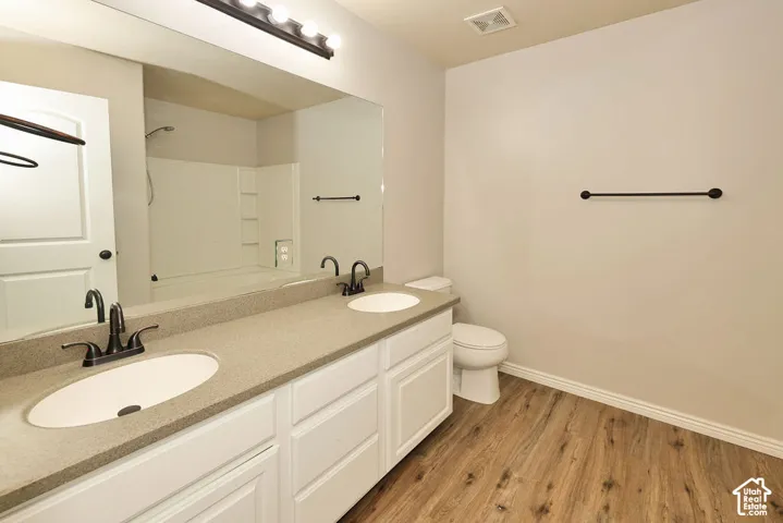 Dual-sink vanity with matte black fixtures, solid-surface countertop, full-width vanity mirror, and wood-finish flooring