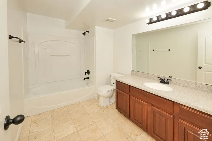 Bathroom featuring stone-tile flooring, a vanity with a solid-surface countertop and integrated sink, a full-width vanity mirror, a tub-shower combination with matte black hardware, and an overhead vanity light fixture