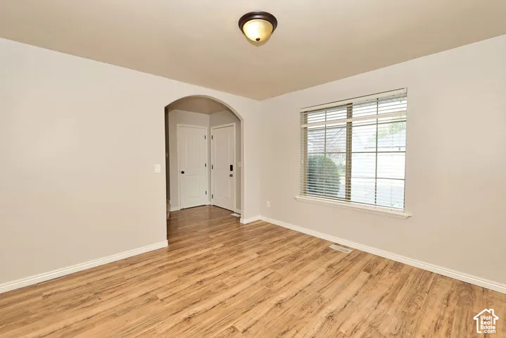 Interior space featuring wood-finish flooring, a neutral color palette, an arched doorway, paneled interior doors, and a window with horizontal blinds