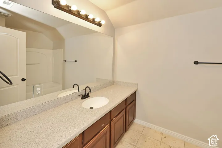 Bathroom featuring a vanity with dark wood-finish cabinetry, stone-composite countertop, integrated sink, matte black faucet, and full-width wall mirror
