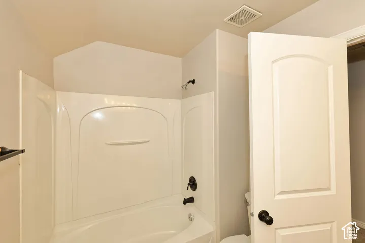 Shower and tub combination with a white molded surround, accented by matte black fixtures, arched interior door with matching hardware, and neutral wall tones