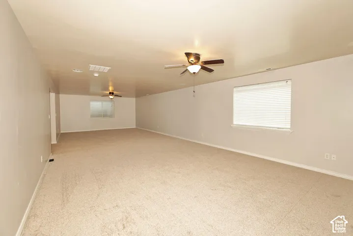 Neutral-toned interior featuring wall-to-wall carpeting, dual ceiling fans with integrated lighting, and horizontal window blinds