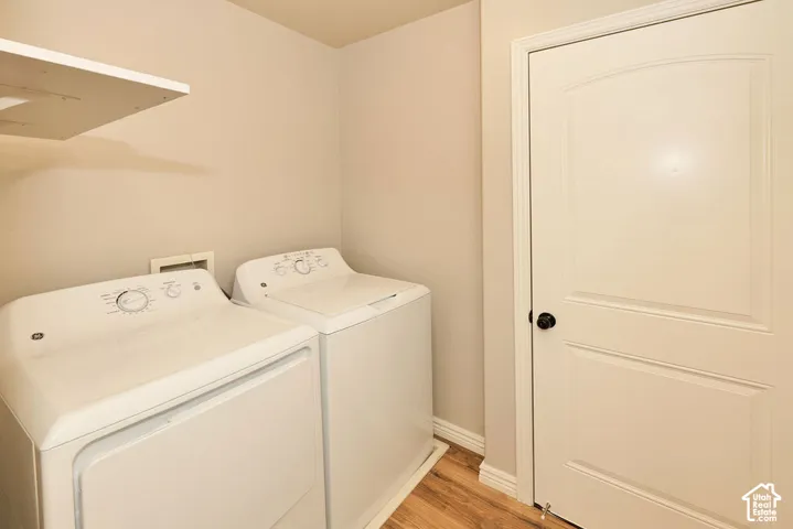 Laundry area featuring wood-finish flooring, a neutral color palette, built-in shelving, and a paneled interior door with matte black hardware