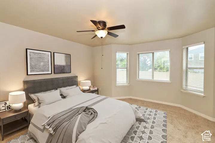Neutral-toned room featuring a bay window, wall-to-wall carpeting, and a ceiling fan with integrated lighting