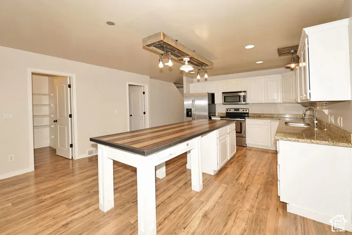 Kitchen featuring white cabinetry, stone-surface countertops, wood-finish flooring, a wood-beam pendant light fixture, and a central island with a wood-plank surface