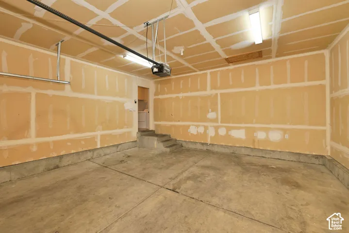 Garage space featuring concrete flooring, taped drywall, overhead fluorescent lighting, and a motorized garage door opener
