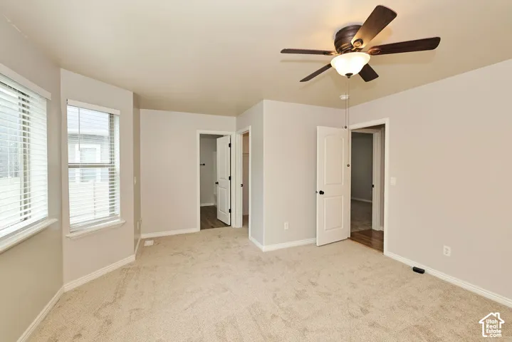 Neutral-toned interior featuring wall-to-wall carpeting, multiple windows, solid-core doors, and a ceiling-mounted light fixture with a fan