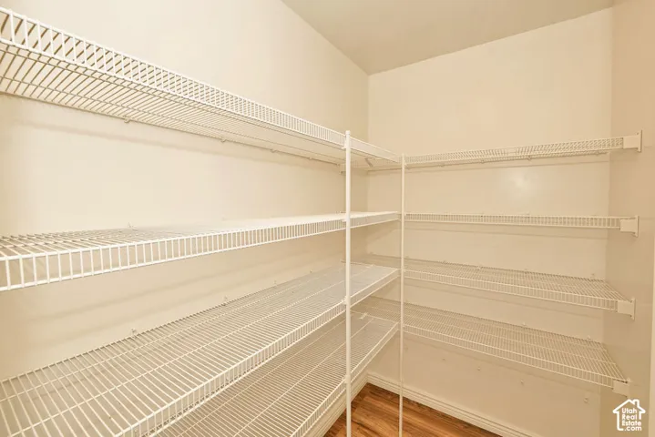 Walk-in storage space featuring multi-tiered white wire shelving and wood-finish flooring