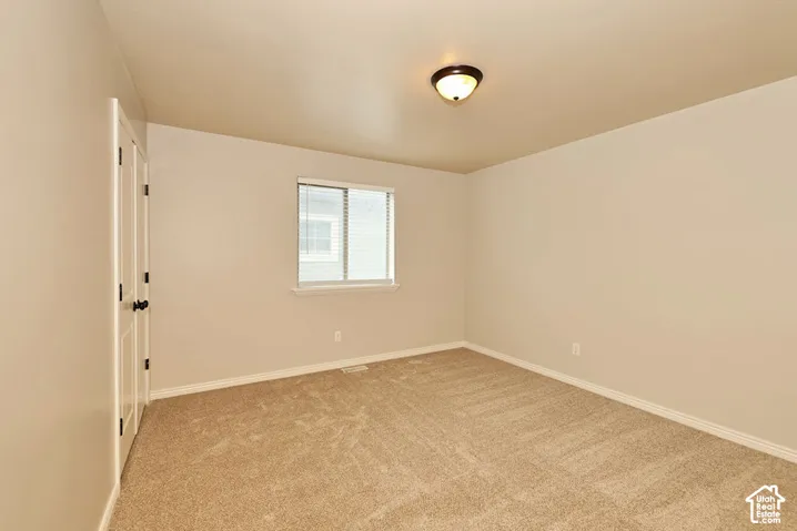 Neutral-toned interior featuring wall-to-wall carpeting, dual-panel closet doors with matte black hardware, a single-pane window, and a flush-mount ceiling light fixture
