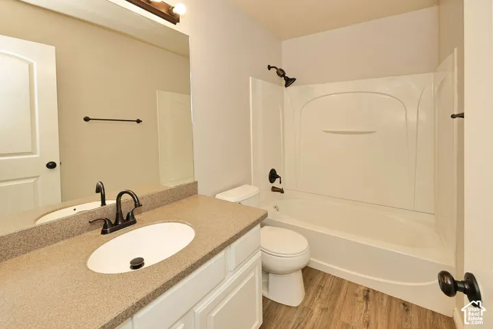 Bathroom featuring a white vanity with a solid surface countertop, integrated oval sink, wood-finish flooring, and matte black fixtures including a wall-mounted light and shower hardware