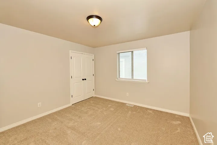 Neutral-toned room featuring carpeting, a sliding window with horizontal blinds, a closet with double doors, and a flush-mount ceiling light fixture