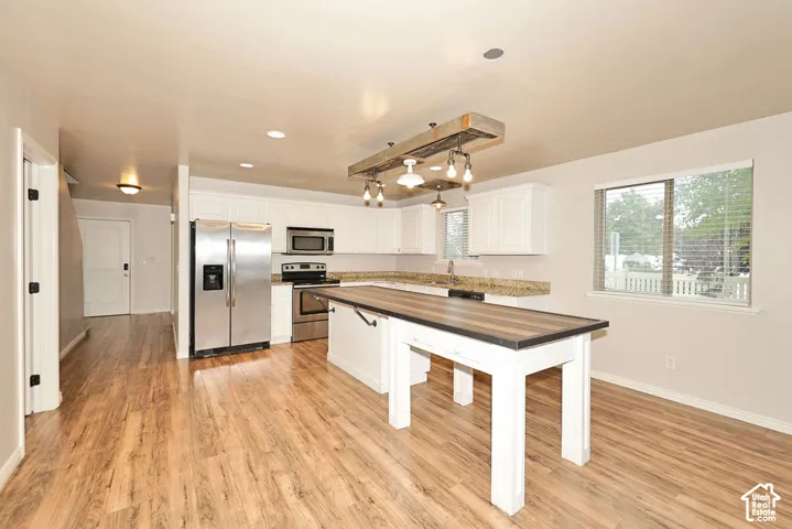 Kitchen featuring white cabinetry, stone-surface countertops, wood-finish flooring, a wood-beam pendant light fixture, and an island with a wood-surface countertop